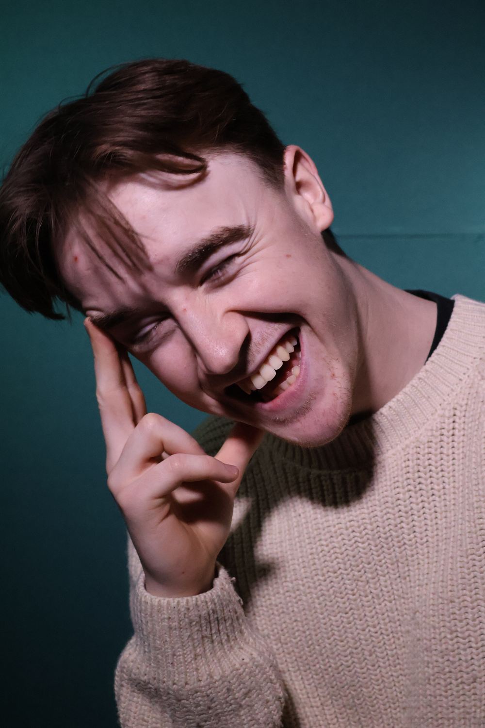 Terance-Joseph Sargent mid-laugh with his head tilted, against a deep teal backdrop
